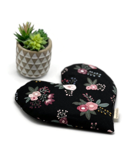 A heart-shaped handmade heating pad with a black floral fabric design, placed next to a small geometric pot containing a green succulent plant.