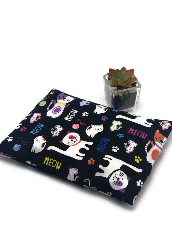 black fabric corn heating pad with cartoon cat and meow signs printed on on a white background
