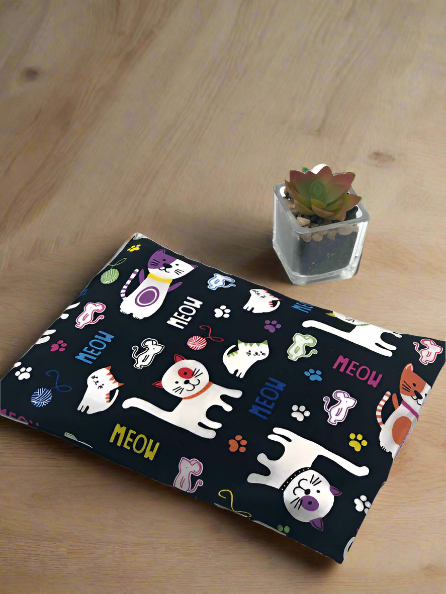 corn heating pad with a black 100% cotton fabric with cartoon cats and meow signs printed on it on a wooden table