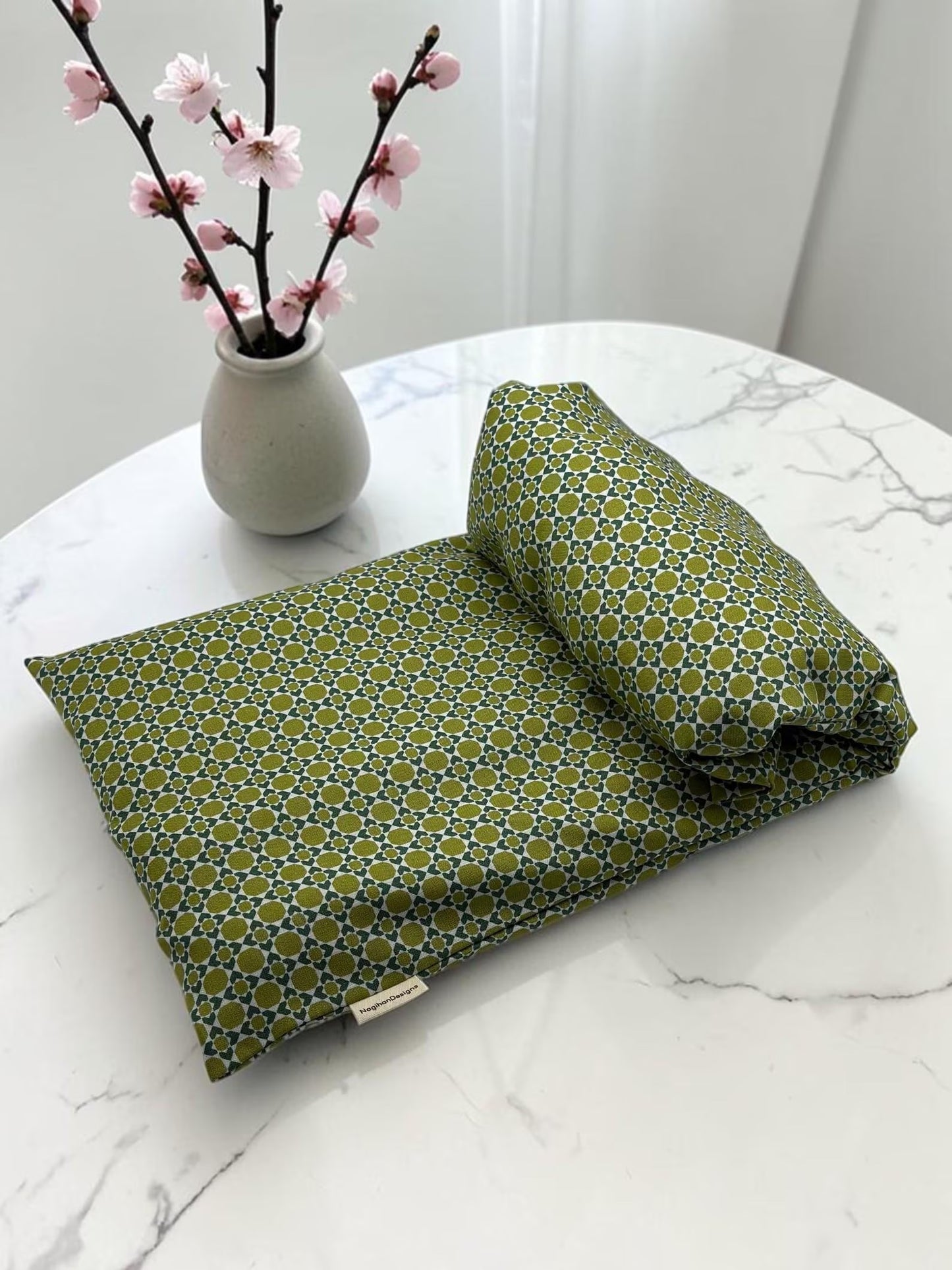 Handmade 8x19 heating and cooling pad with eye pillow in olive green geometric print cotton, styled on marble with cherry blossoms
