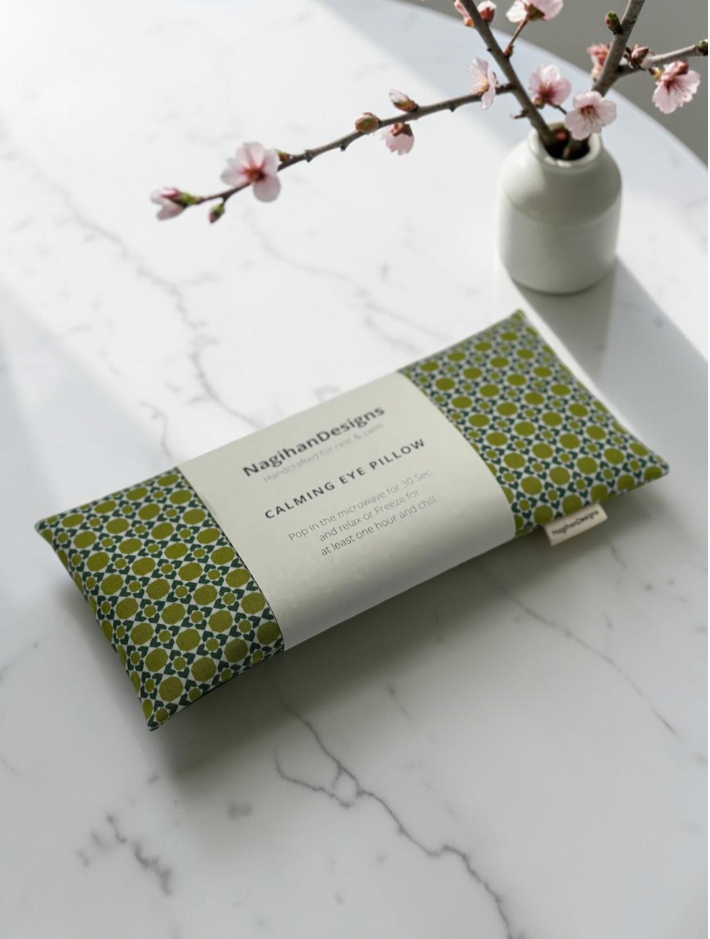 Calming Eye Pillow in olive green geometric print cotton with NagihanDesigns label, styled on marble with cherry blossoms
