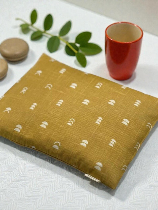 Yellow fabric with white patterns on a white surface with a red cup and green leaves.
