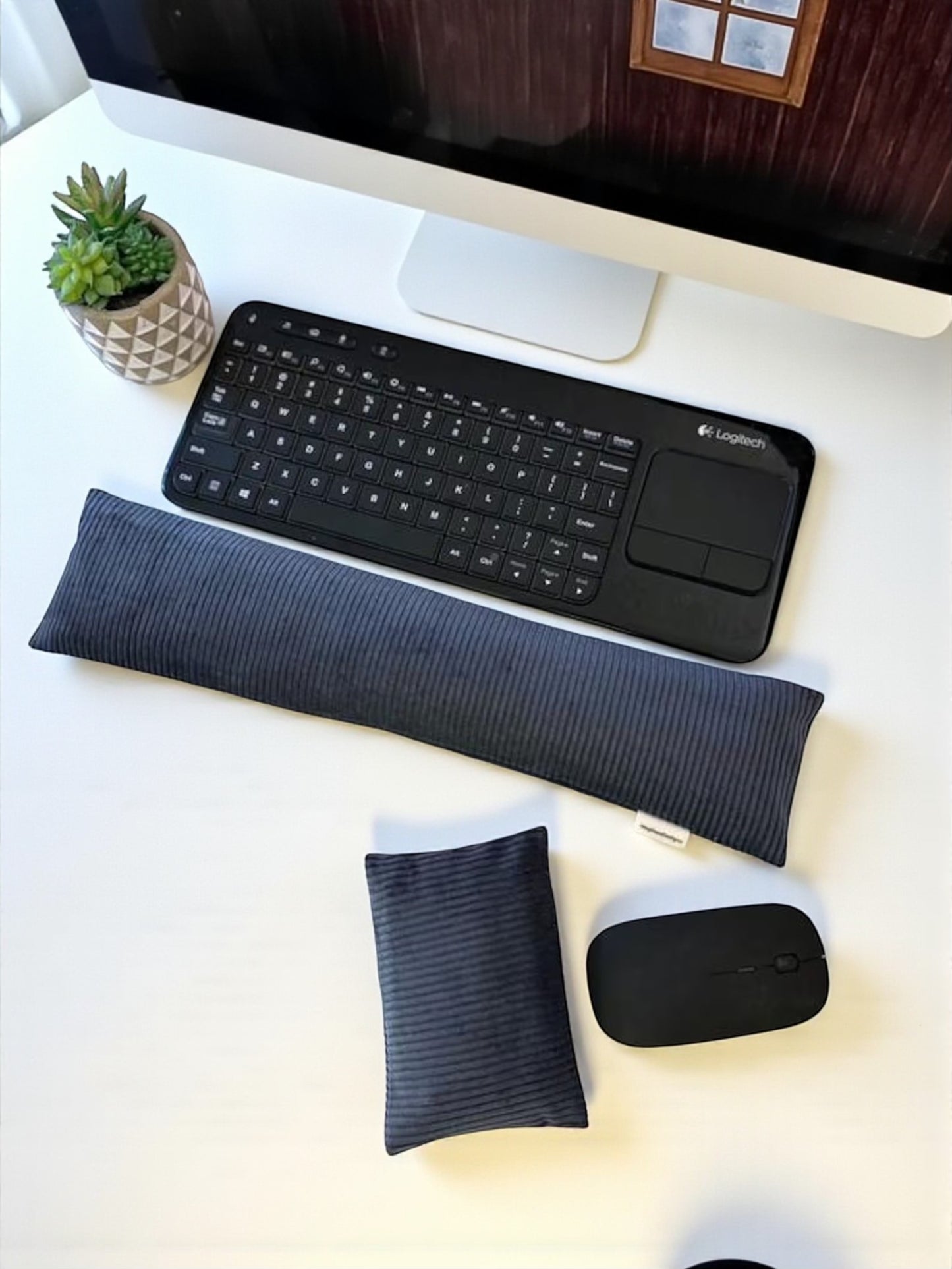 Black keyboard, wrist rest, and mouse on a white desk with a computer monitor in the background.