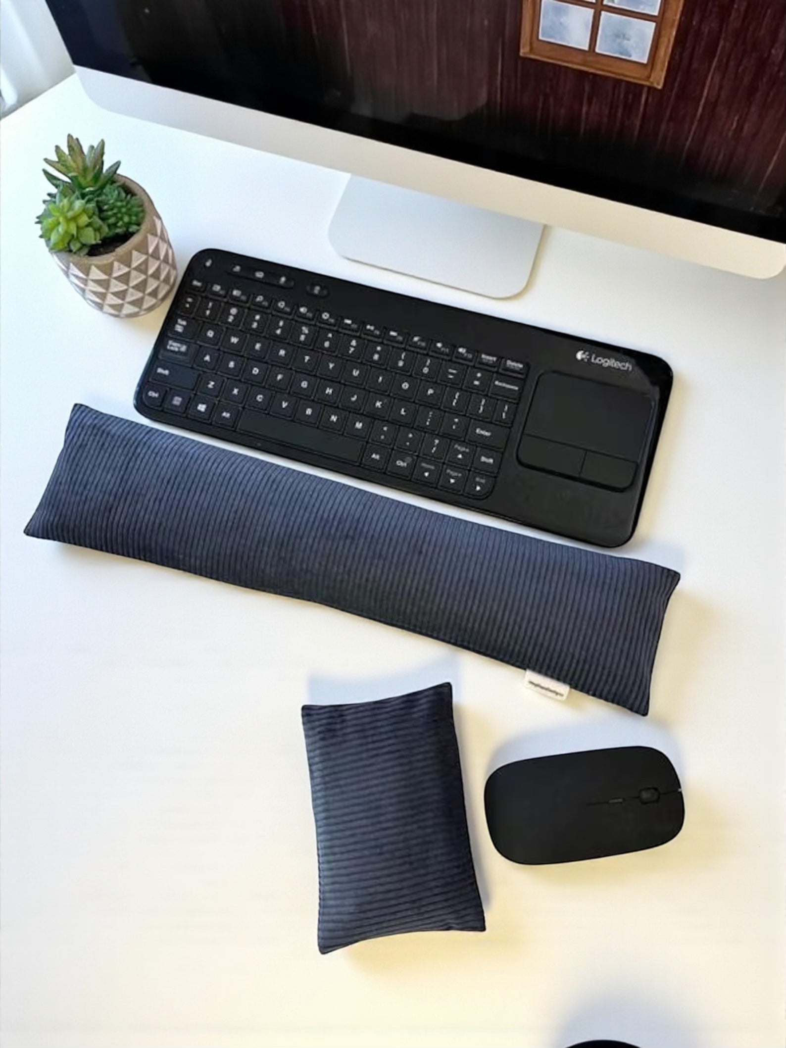 Black keyboard, wrist rest, and mouse on a white desk with a computer monitor in the background.
