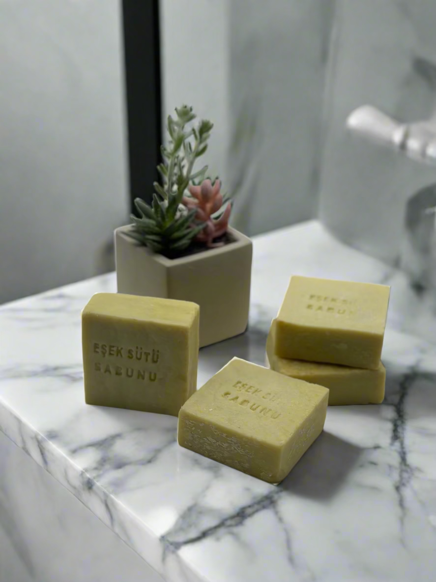 Three green bars of soap with a small plant in the background on a white surface