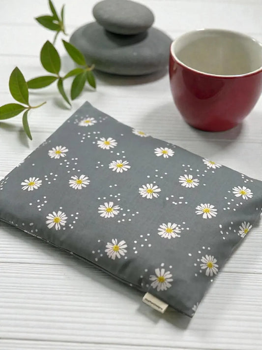 Gray fabric with white floral pattern on a white surface with a red cup and green leaves.