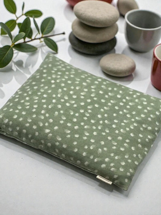 Green fabric pouch with white patterns on a white surface with stones and a plant.
