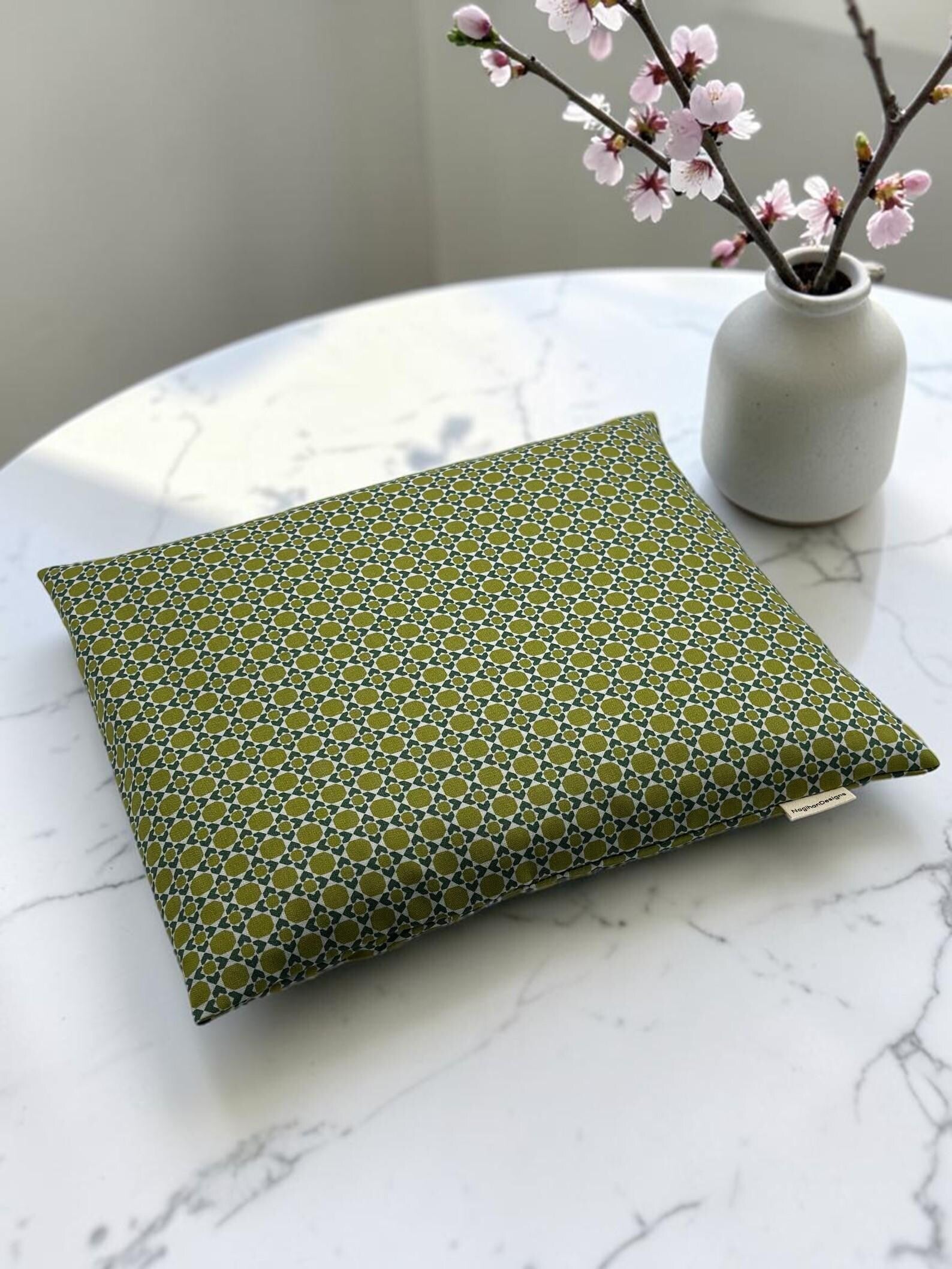 Handmade heating and cooling pad in olive green geometric print cotton, 9x11 inches, styled on marble with cherry blossoms