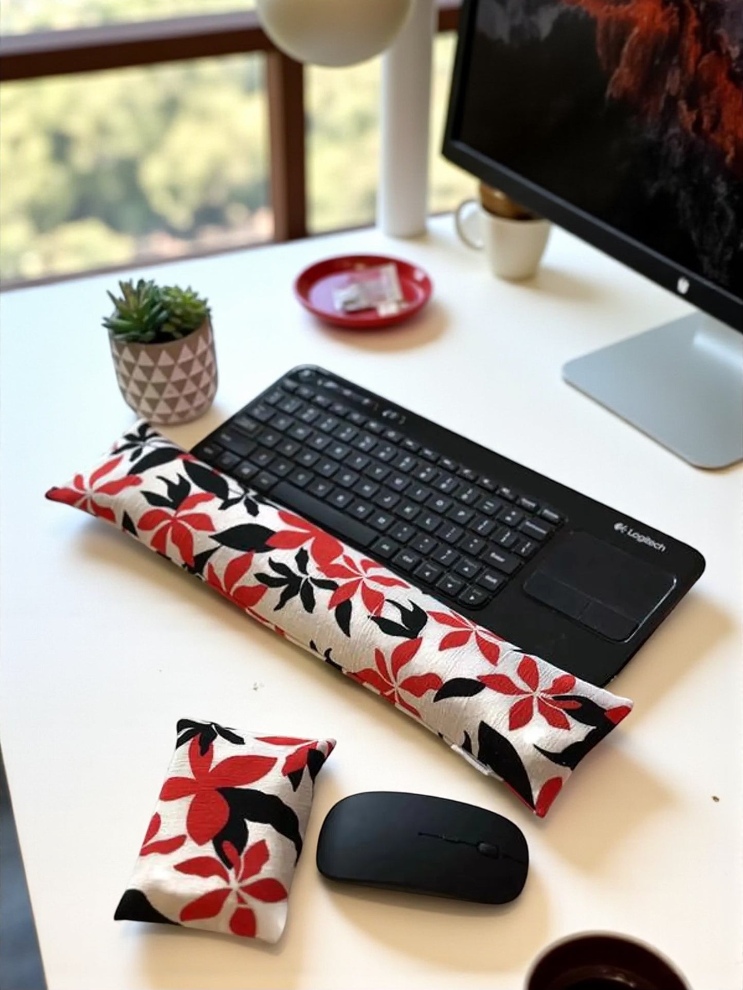 Decorative keyboard rest with red and black floral pattern on a desk with computer and accessories.