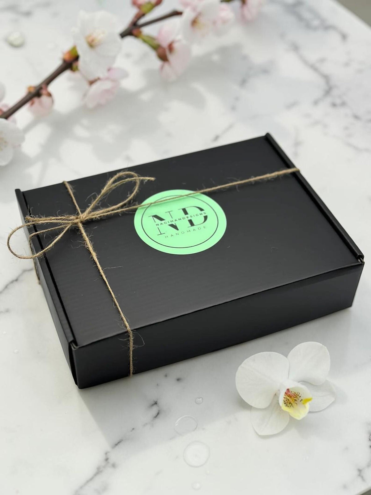 NagihanDesigns black gift box with twine bow and branded sticker on a marble surface with white flowers