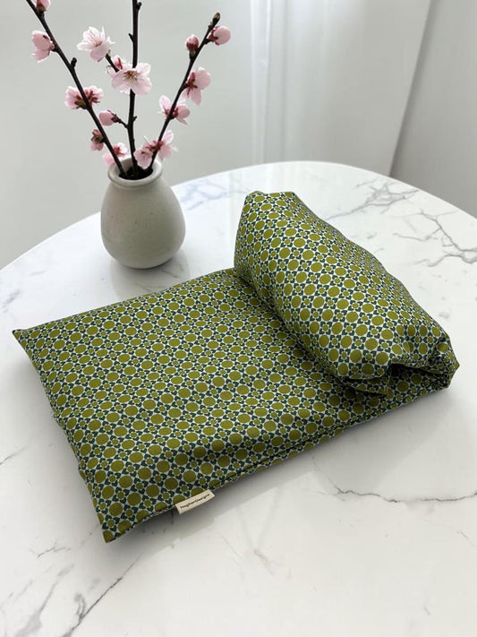 NagihanDesigns olive green geometric print cotton heating and cooling pad on a white marble table with cherry blossoms.
