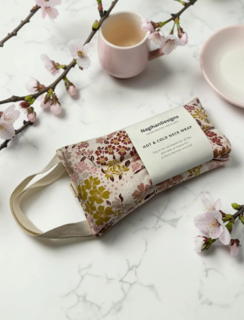 Floral-patterned hot and cold neck wrap with cherry blossoms on a marble surface