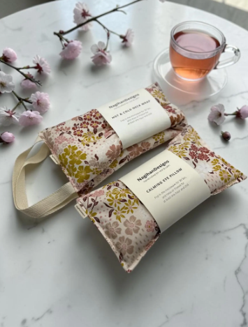 Two floral-patterned rice balls with straps on a marble surface with a cup of tea and cherry blossoms.