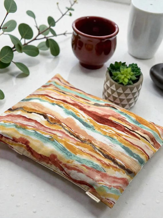 Colorful striped pouch on a white surface with a cup, plant, and small pot in the background.