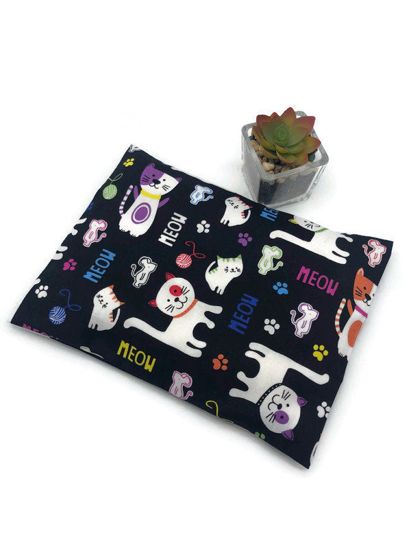 black fabric corn heating pad with cartoon cat and meow signs printed on with a white background 